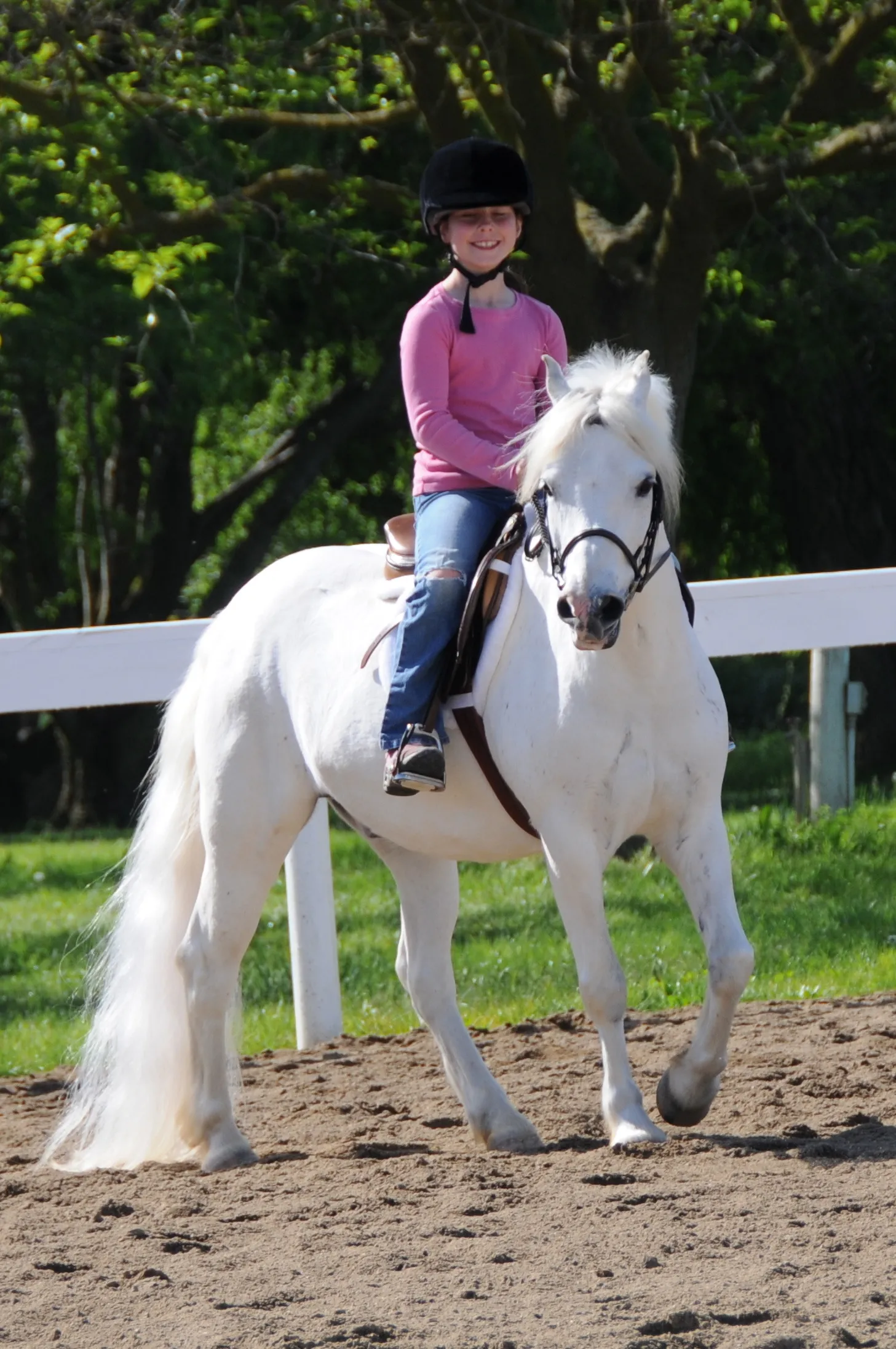 A young rider smiling aboard a white pony in the arena